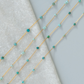 Gold chain necklace with turquoise beads on a textured surface