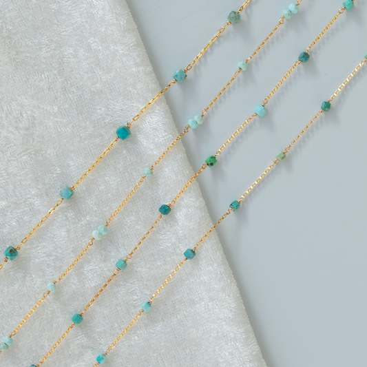 Gold chain necklace with turquoise beads on a textured surface