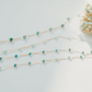 Gold chain necklace with turquoise beads on a light gray background