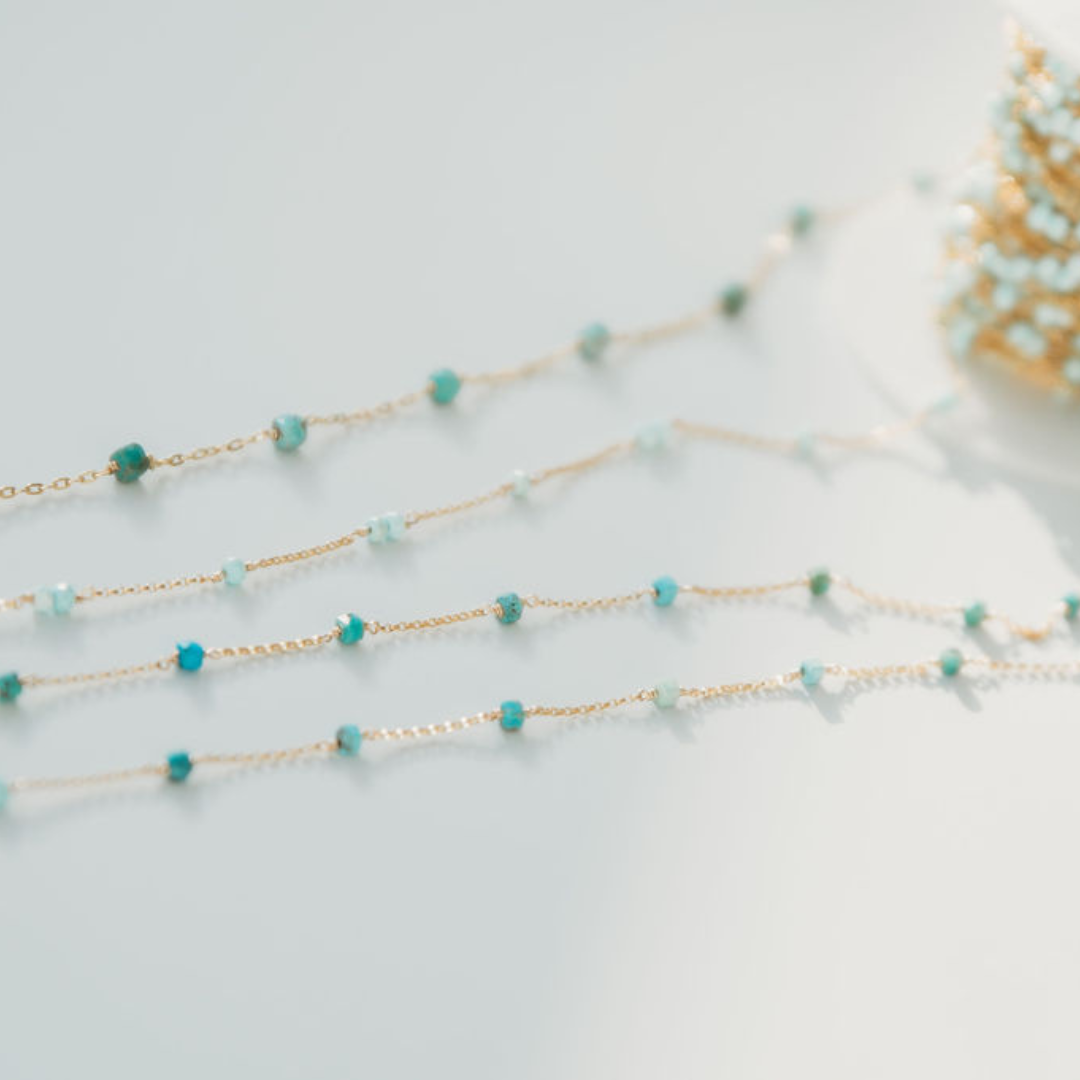 Gold chain necklace with turquoise beads on a light gray background
