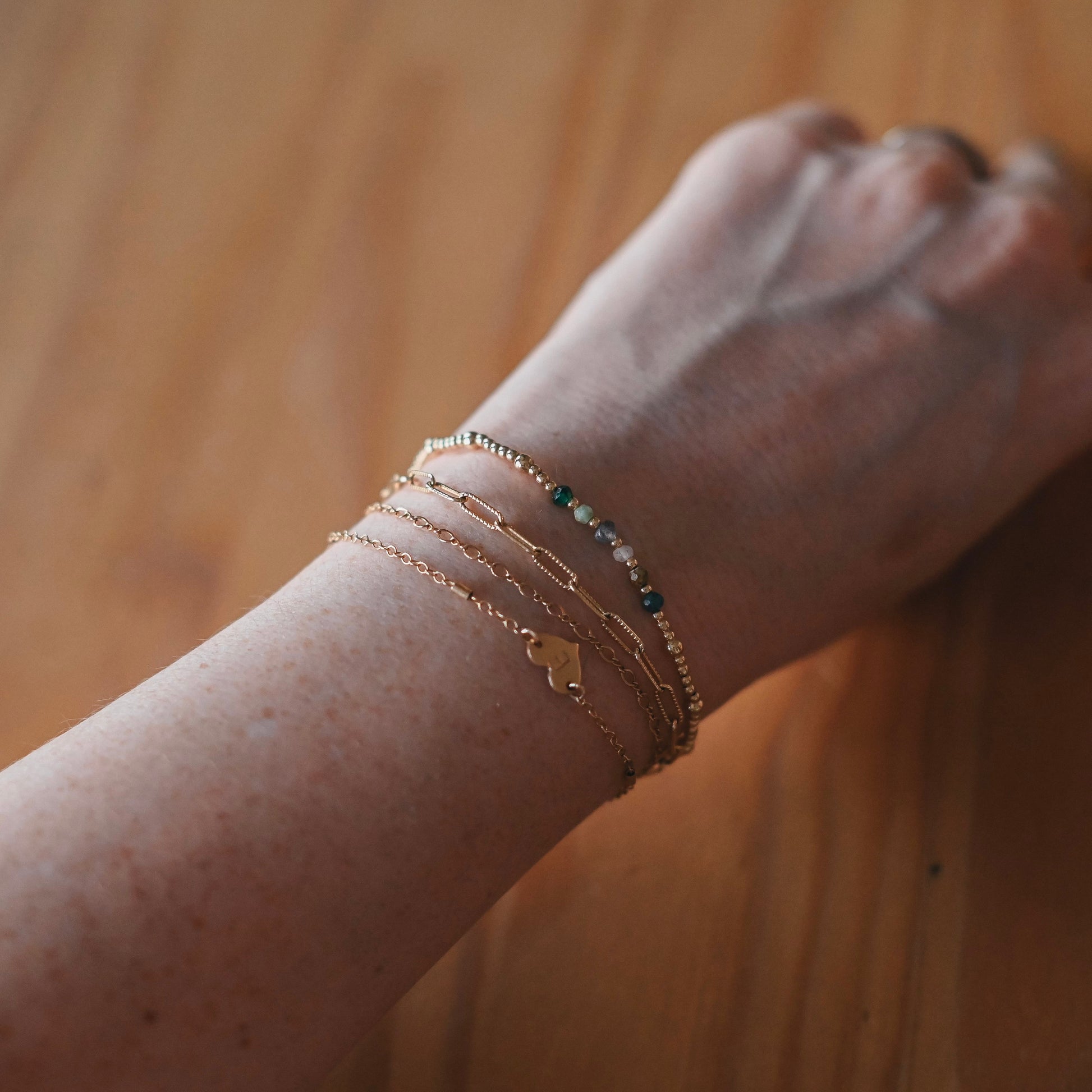 Close-up of a wrist wearing multiple gold bracelets on a wooden surface