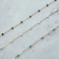 Gold chain necklace with green and blue beads on a marble surface