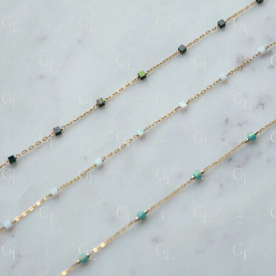 Gold chain necklace with green and blue beads on a marble surface