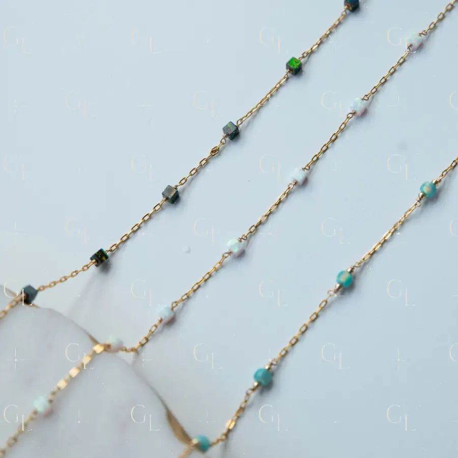 Gold chain necklace with green and blue gemstones on a light blue background