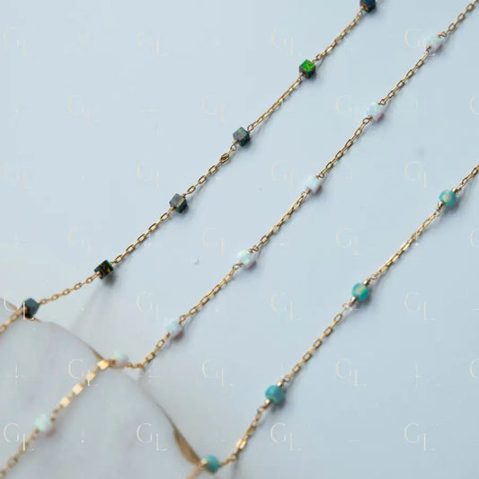 Gold chain necklace with green and blue gemstones on a light blue background