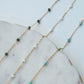 Gold chain necklace with turquoise and green beads on a marble surface