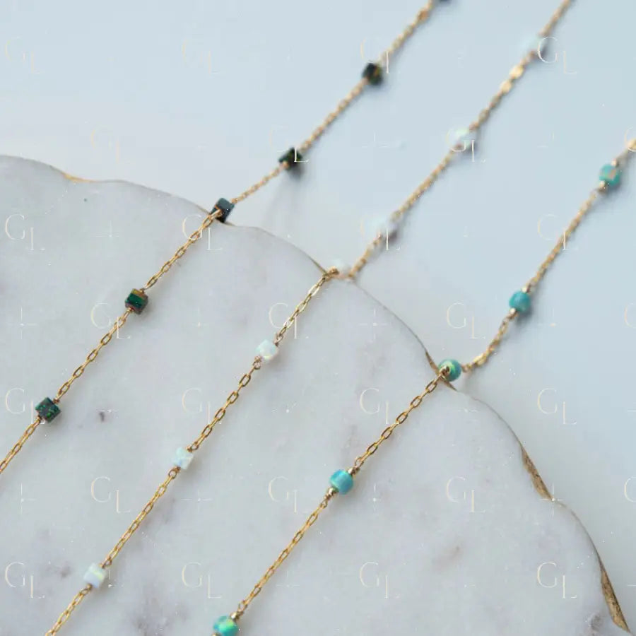 Gold chain necklace with turquoise and green beads on a marble surface