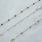 Gold chain necklace with green and blue beads on a marble surface