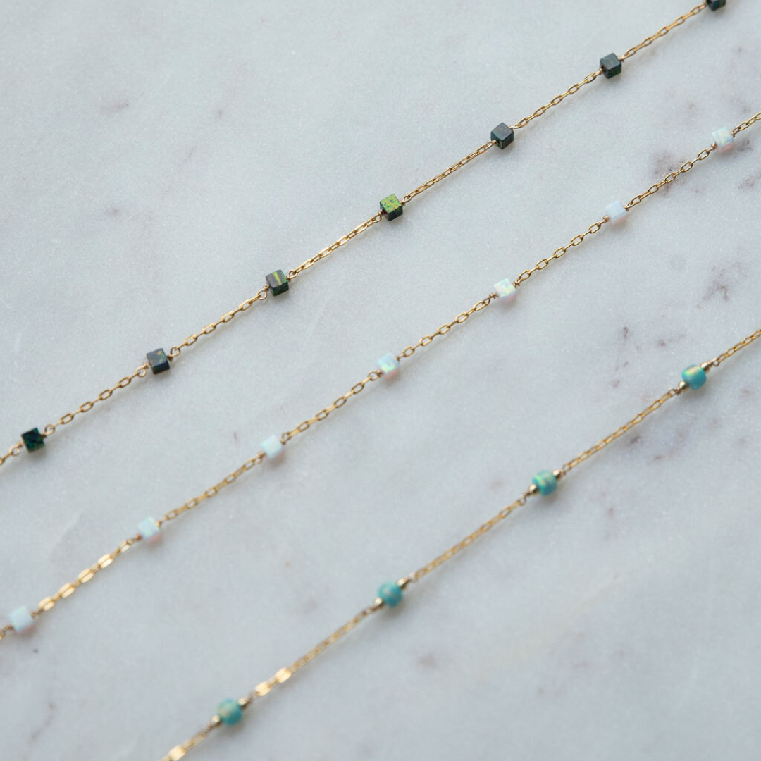 Gold chain necklace with green and blue beads on a marble surface