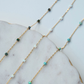 Gold chain necklace with turquoise and green beads on a marble surface