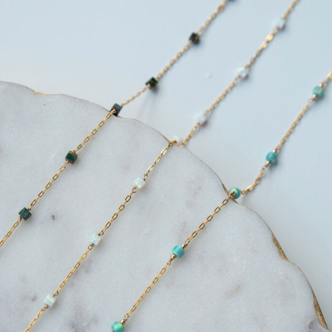 Gold chain necklace with turquoise and green beads on a marble surface