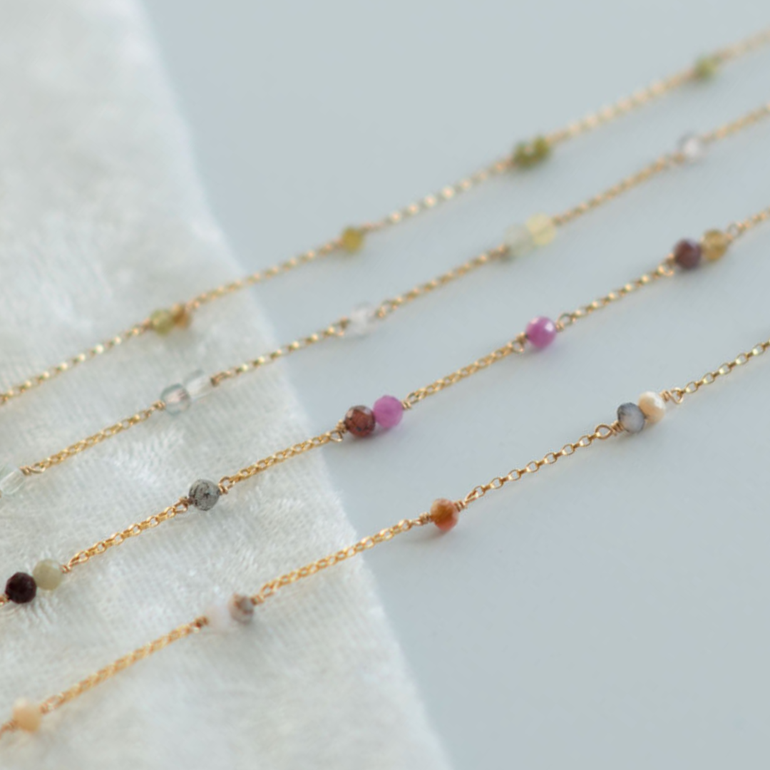 Gold necklaces with small beads on a white fabric background