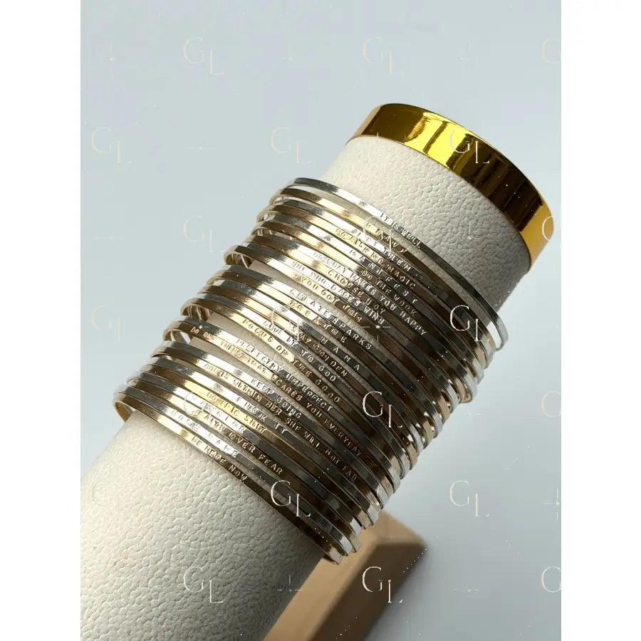 Set of silver bangles on a white cylindrical stand with gold accents against a light gray background