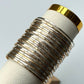 Set of silver bangles on a white cylindrical stand with gold accents against a light gray background