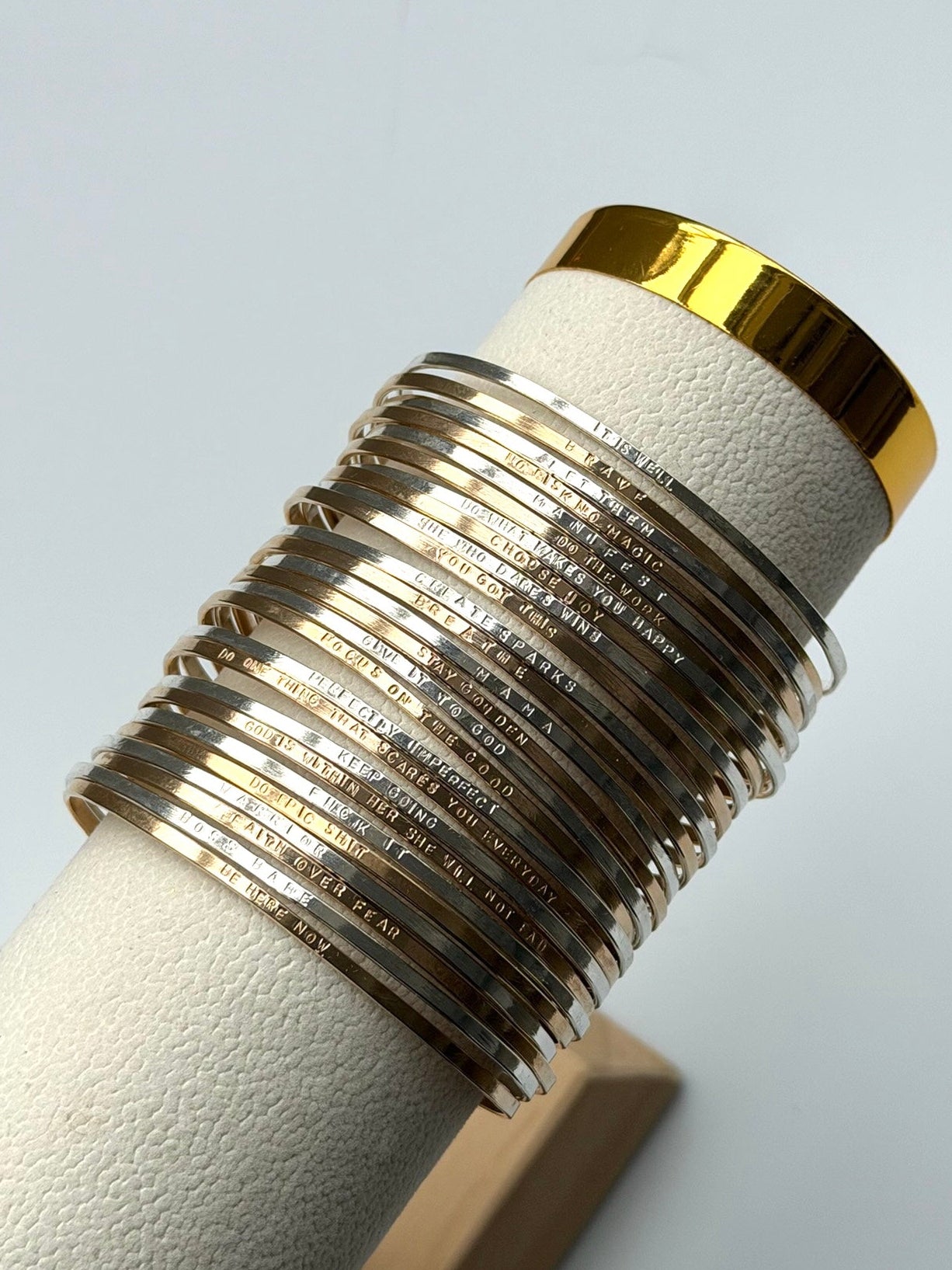 Set of silver bangles on a white cylindrical stand with gold accents against a light gray background