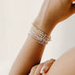 Hand wearing multiple pearl bracelets on a light background