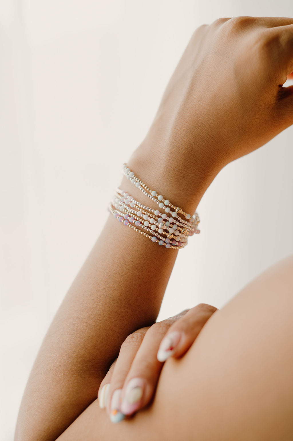 Hand wearing multiple pearl bracelets on a light background