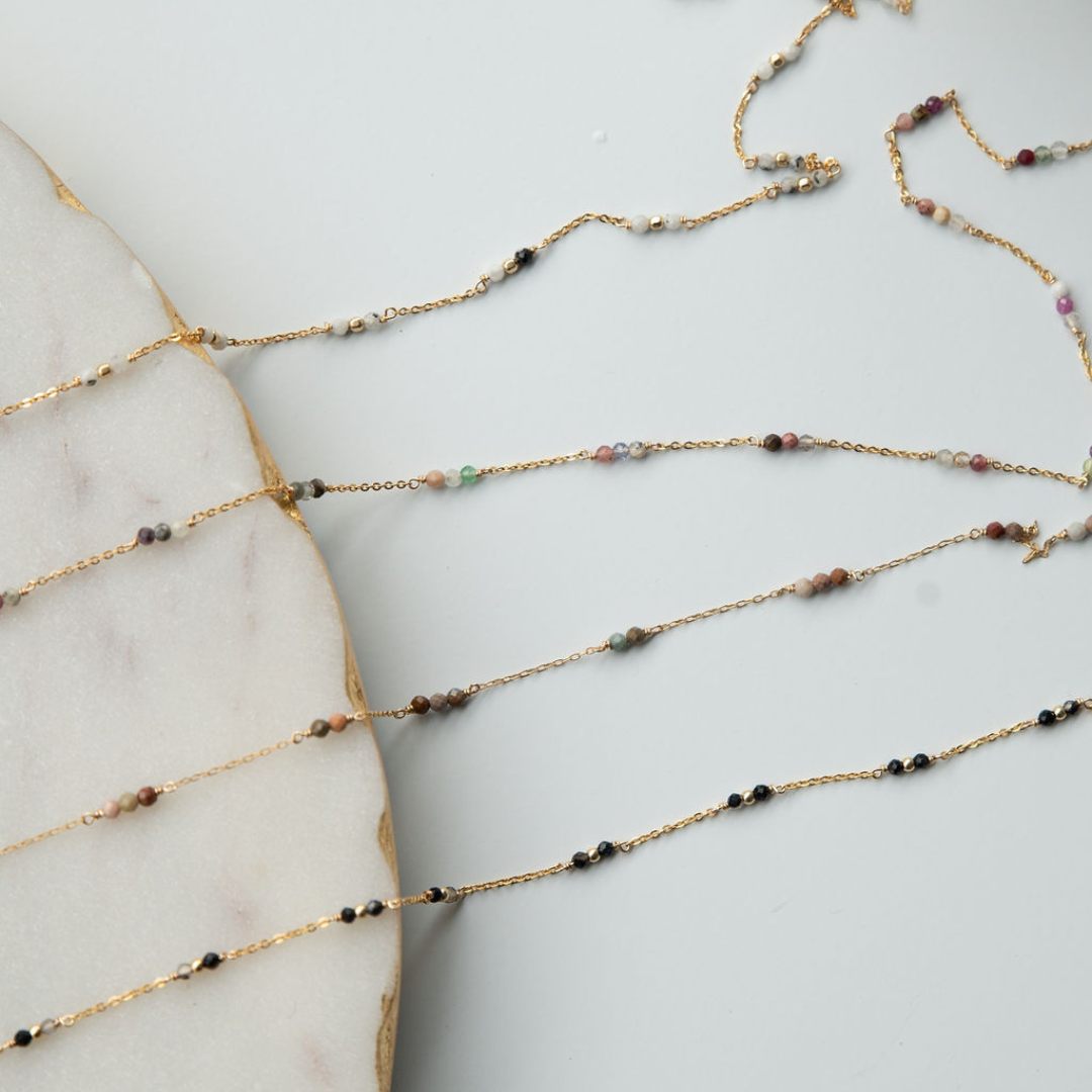 Gold chain necklace with small beads on a marble surface