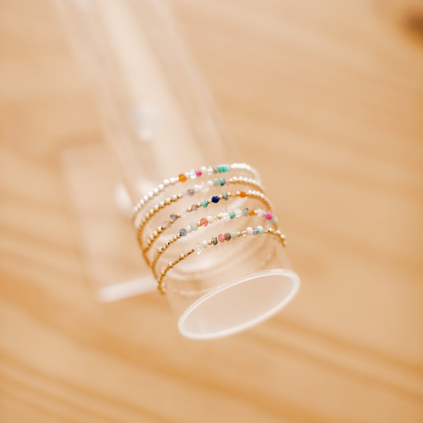 Set of colorful beaded bracelets on a clear stand with a blurred wooden background