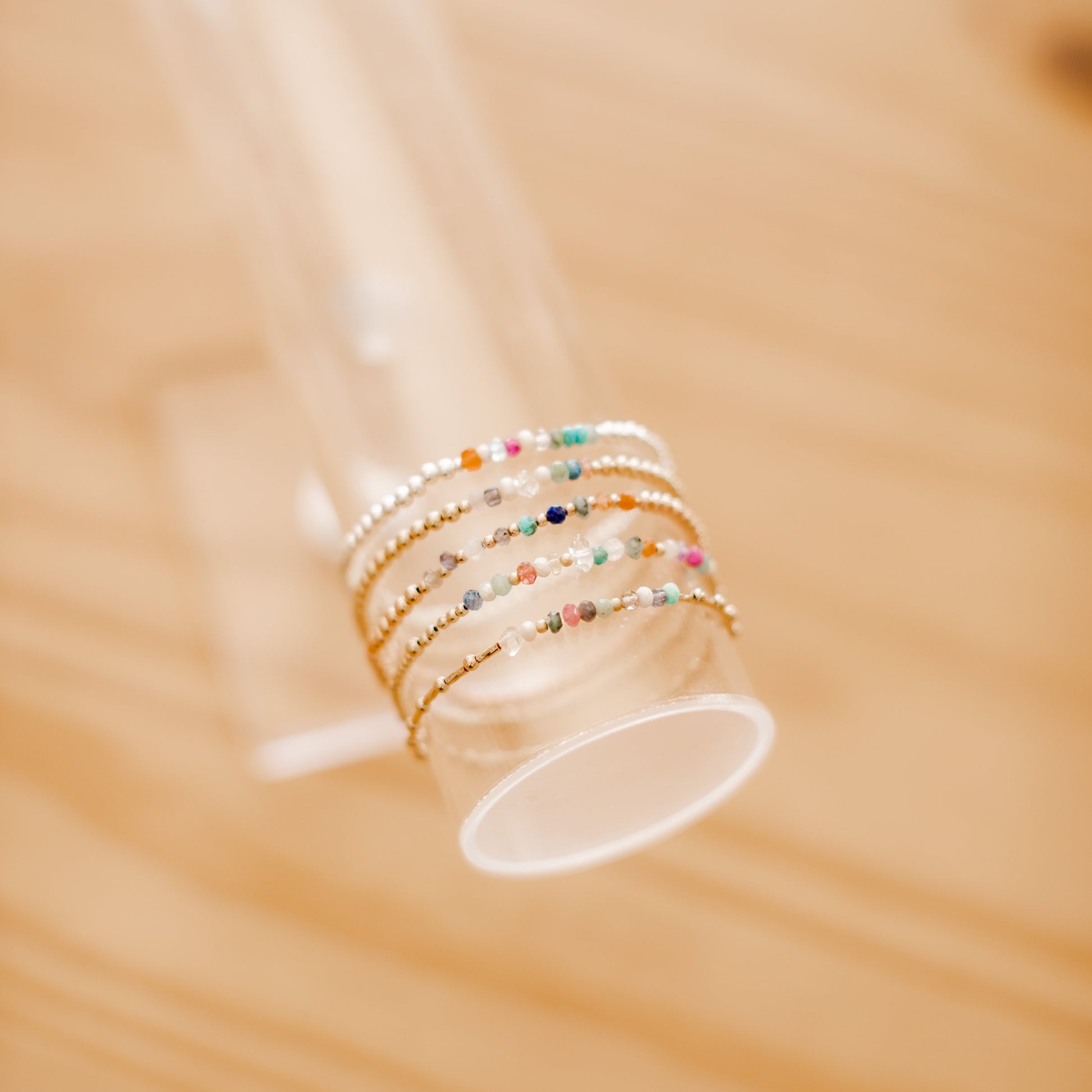 Set of colorful beaded bracelets on a clear stand with a blurred wooden background