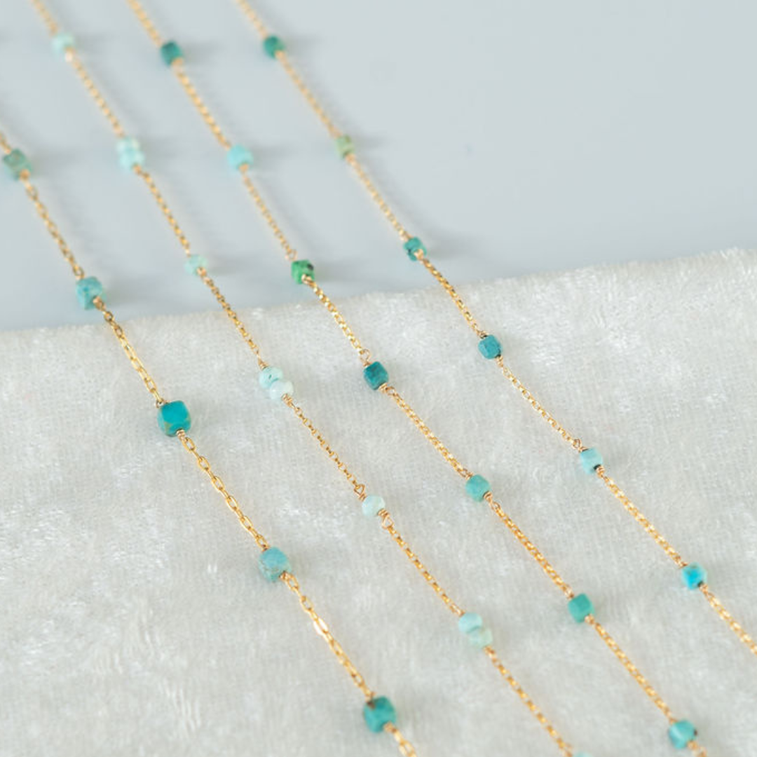 Gold chain with turquoise beads on a textured surface