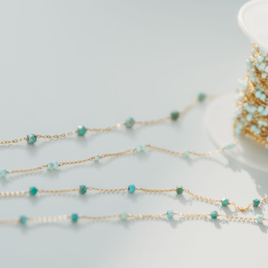 Gold chain with turquoise beads on a light gray background