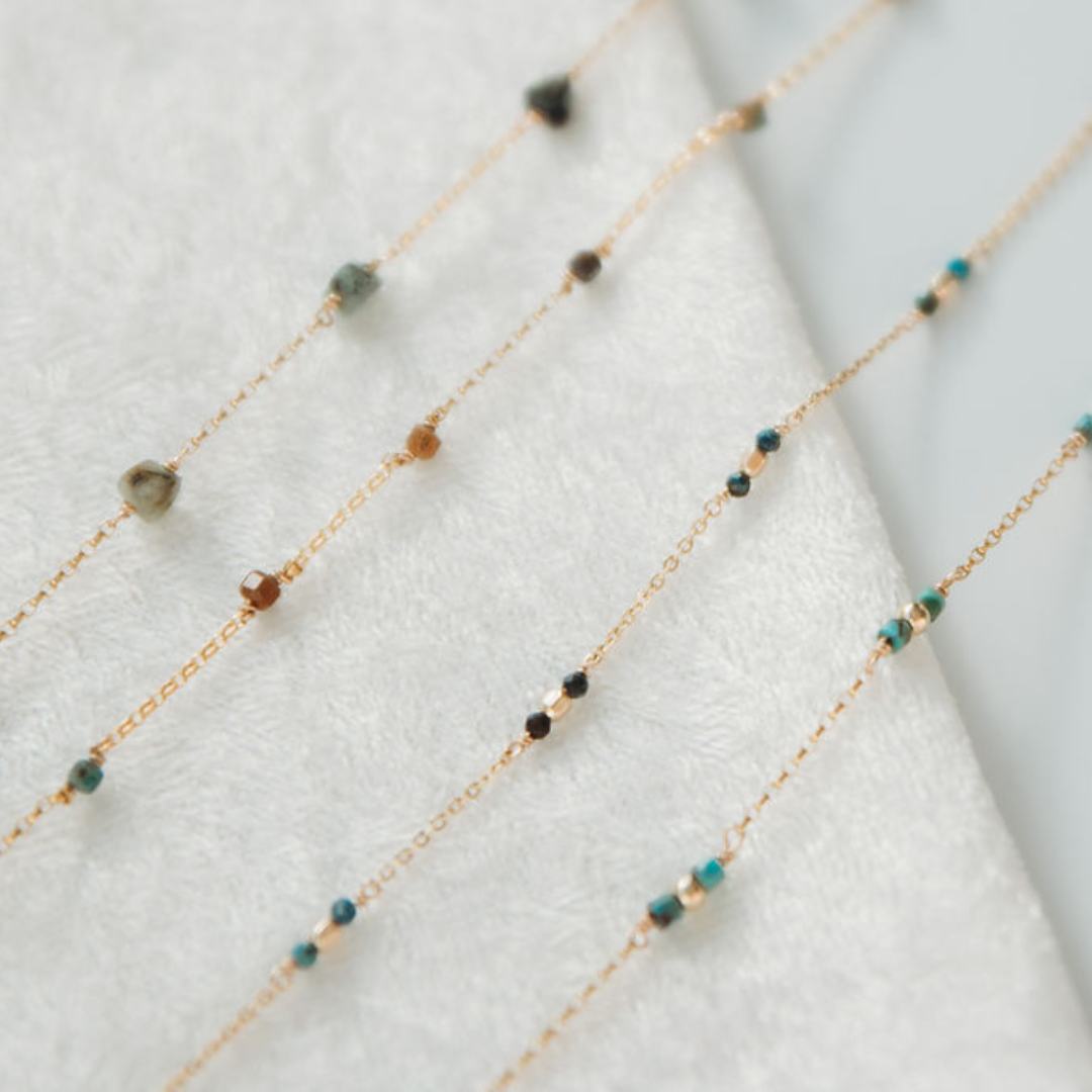 Delicate gold necklace with small beads on a white fabric background