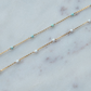 Gold chain necklace with turquoise and white beads on a marble surface