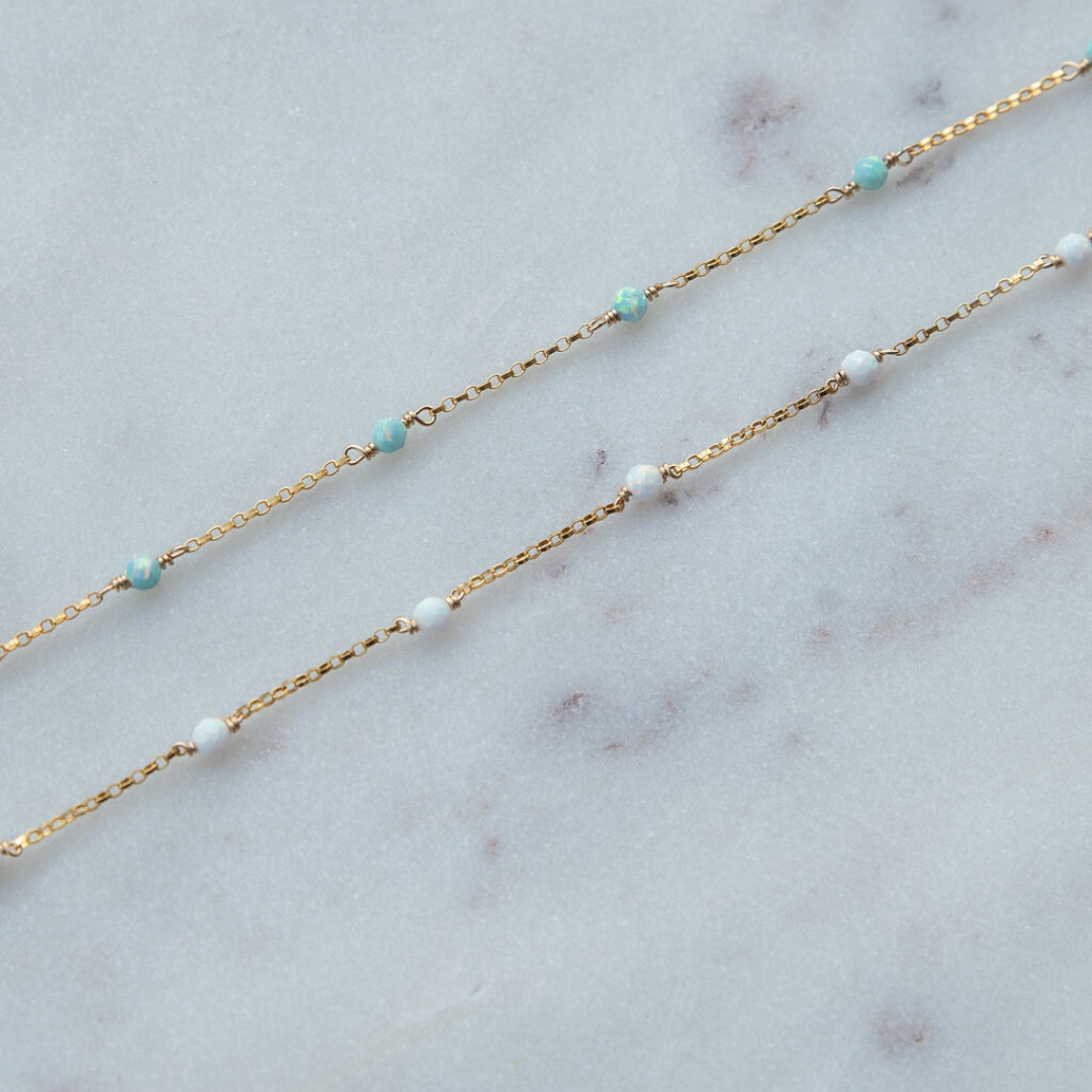 Gold chain necklace with turquoise and white beads on a marble surface