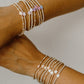 Two arms wearing multiple beaded bracelets on a neutral background