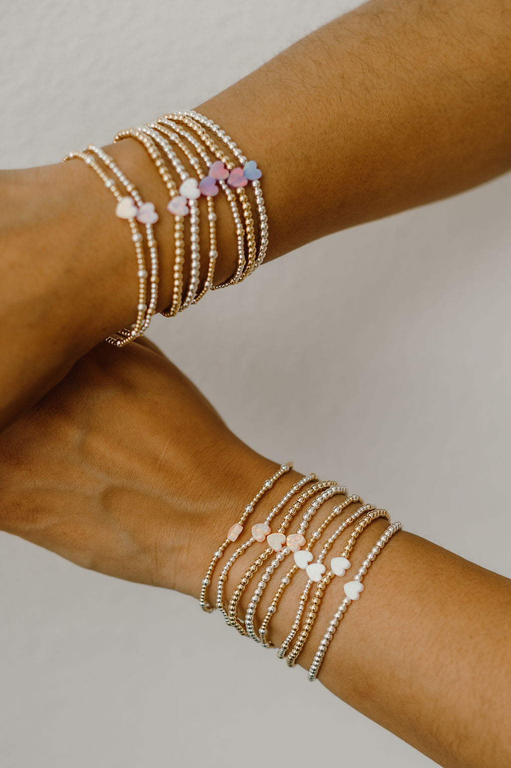 Two arms wearing multiple beaded bracelets on a neutral background