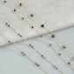 Gold chain necklace with green and brown beads on a light gray background