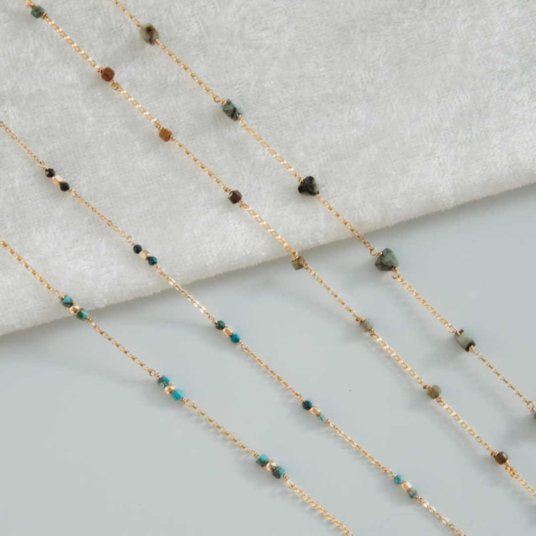 Gold chain necklace with green and brown beads on a light gray background