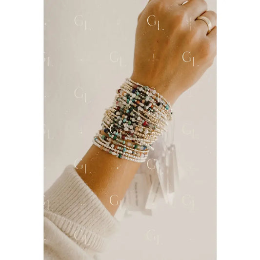 Hand wearing multiple beaded bracelets on a neutral background