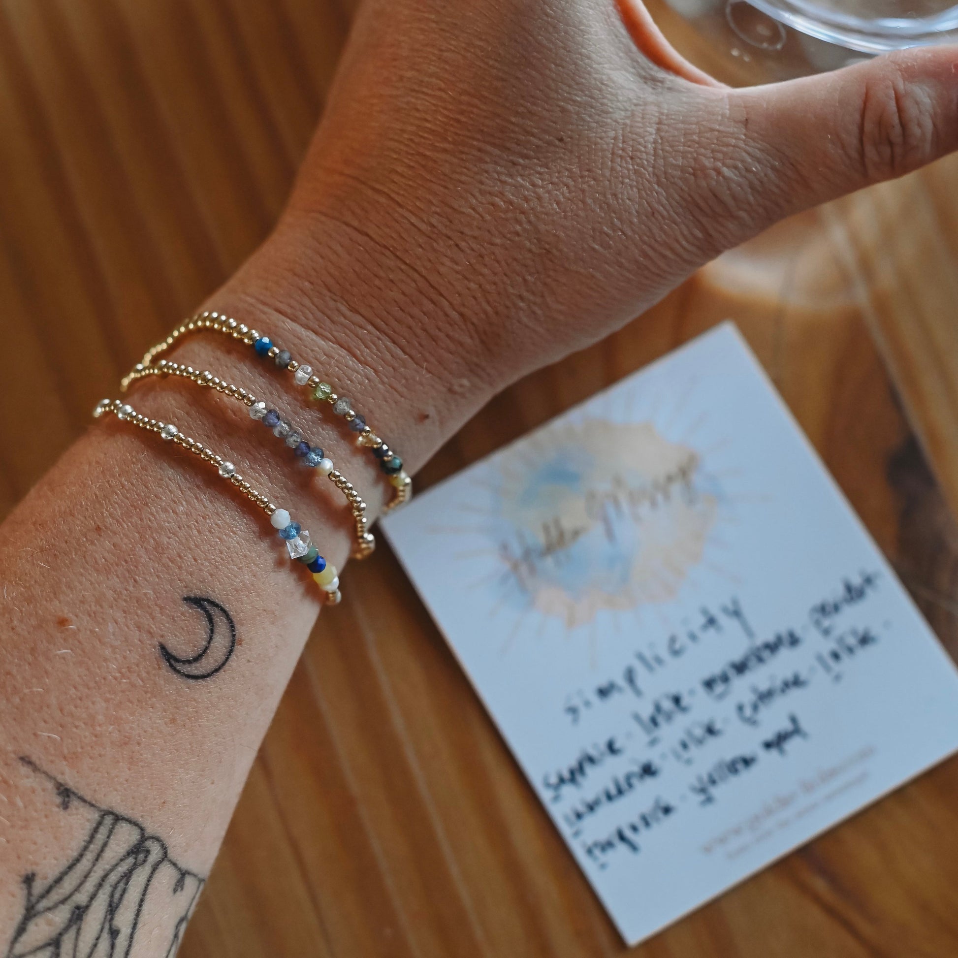 Hand wearing multiple gold bracelets with a card and glass of tea in the background