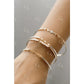 Close-up of a wrist wearing multiple gold and silver bracelets on a neutral background