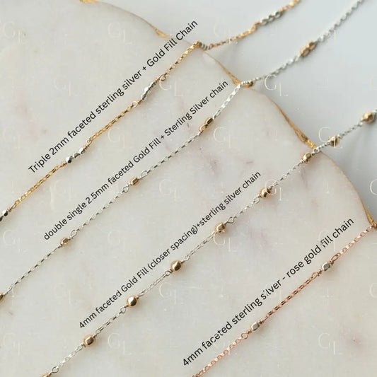 Collection of gold and silver chains on a marble surface with labels.