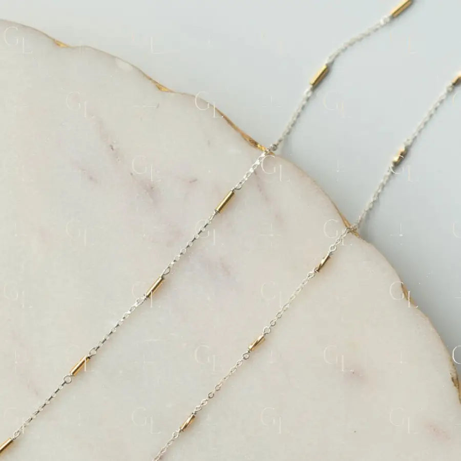 Close-up of a delicate gold and silver chain on a marble surface
