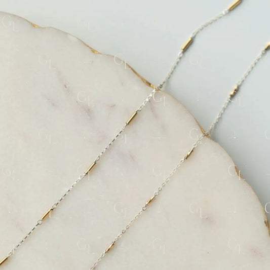 Close-up of a delicate gold and silver chain on a marble surface