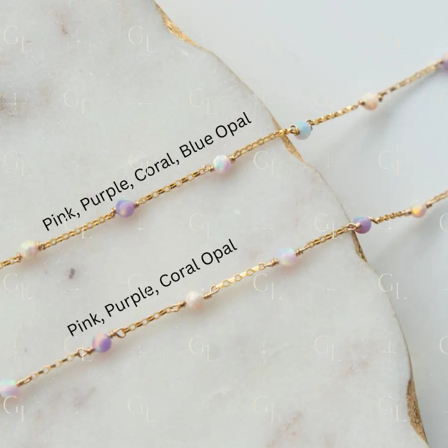 Two gold necklaces with pink, purple, and coral opal beads on a marble surface.