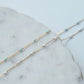 Two gold necklaces with opal blue  and white beads on a marble surface