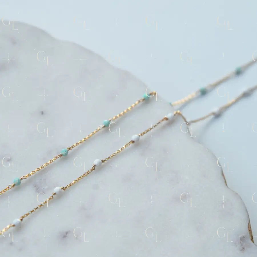 Two gold necklaces with opal blue  and white beads on a marble surface