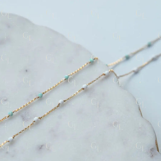 Two gold necklaces with opal blue  and white beads on a marble surface
