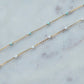 Gold chain necklace with turquoise and white beads on a marble surface