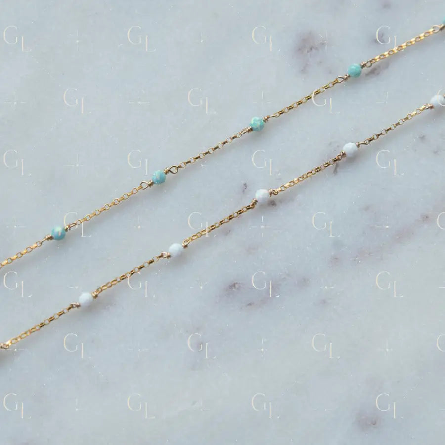 Gold chain necklace with turquoise and white beads on a marble surface