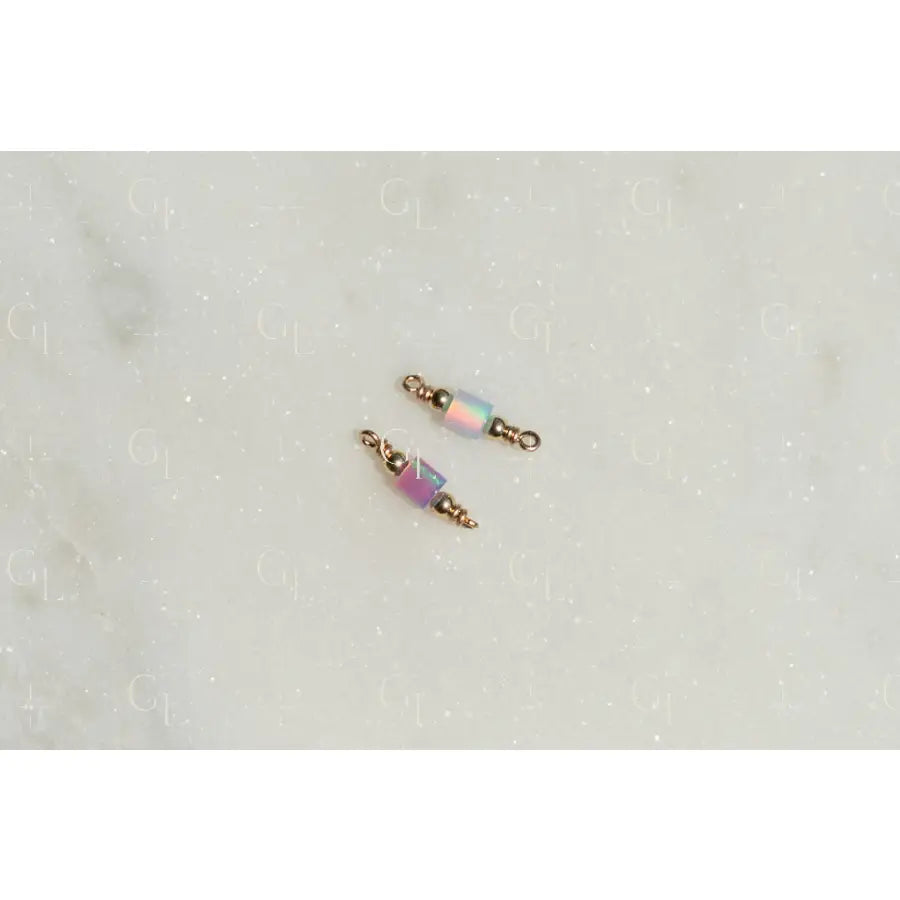 Two gold and pink beaded connectors on a light gray background