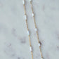 Gold chain necklace with white beads on a marble surface