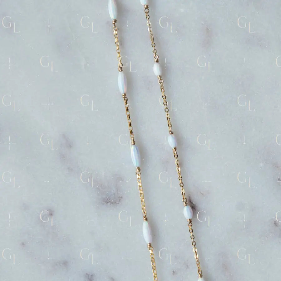 Gold chain necklace with white beads on a marble surface