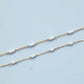 Gold chain with white beads on a light blue background