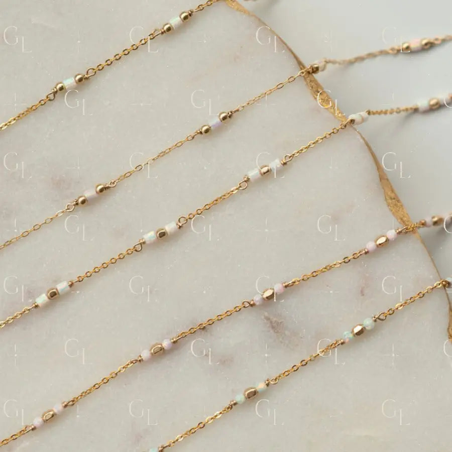 Gold chain necklaces with small beads on a marble surface